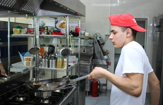 Food handler in kitchen with a frying pan