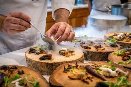 Chef adding ingredients to plated dish with mushrooms