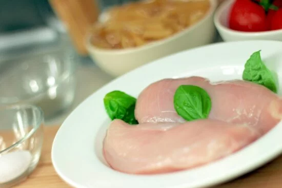 Raw chicken breast on plate with basil leaves
