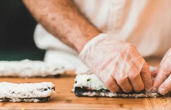 Person wearing gloves preparing sushi rolls